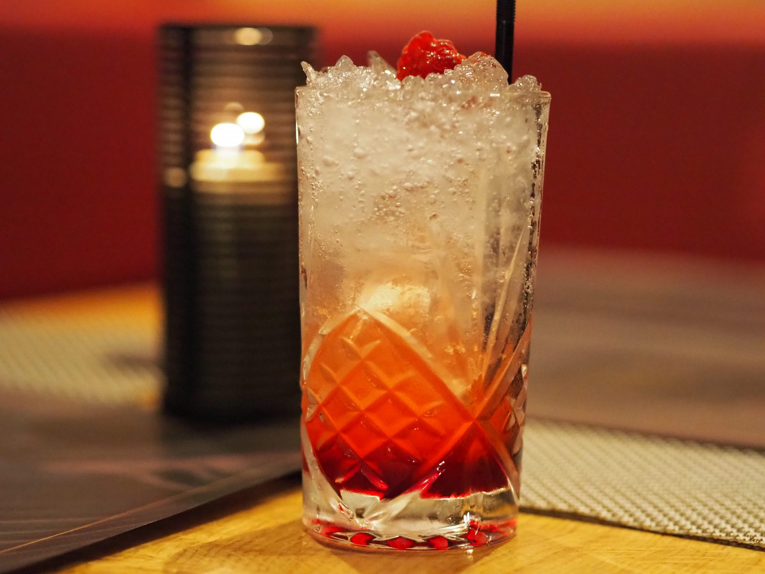 red and white drink with raspberry in front of candlelight